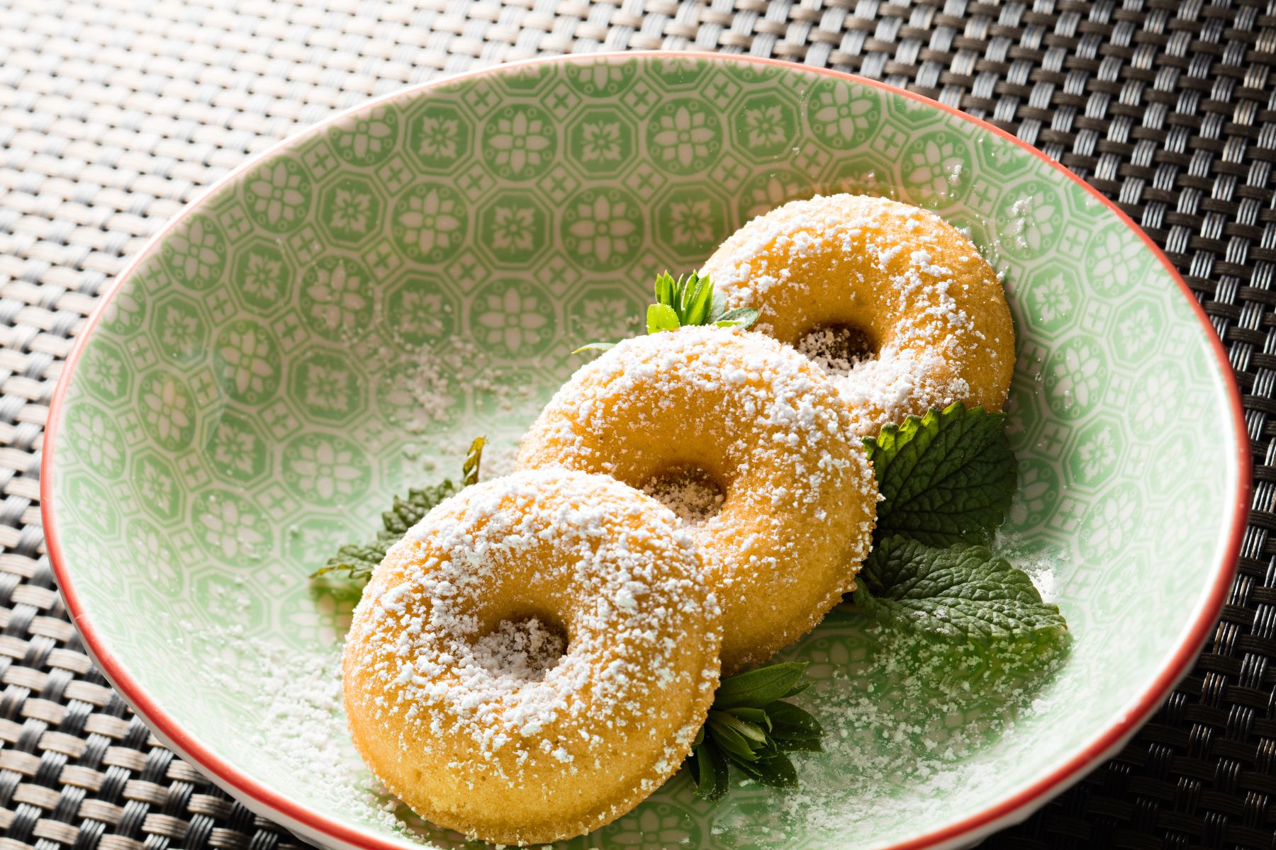 Yeşil bir tabak üzerinde 3 adet donut bulunmaktadır. Donutların üzerine toz hindistan cevizi serpilmiştir.